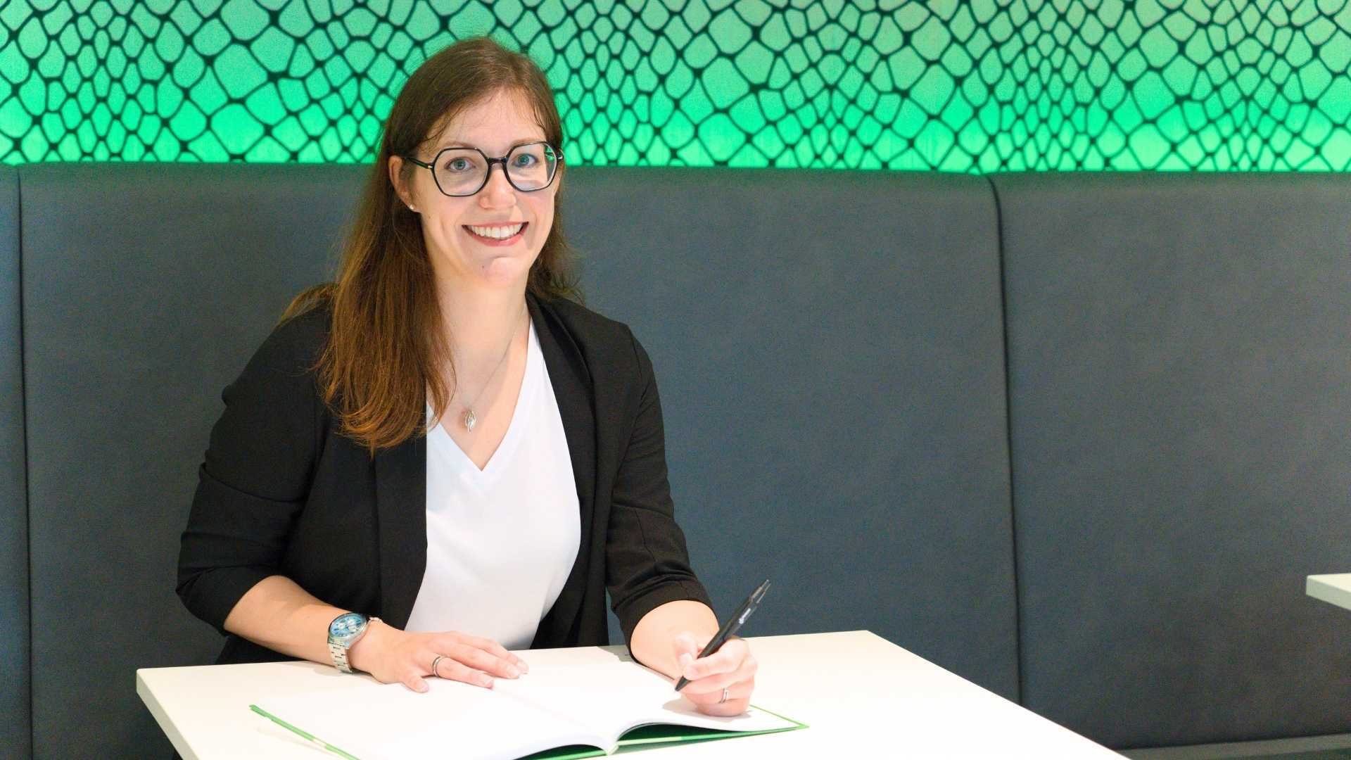 Karina Schloms sitzt an einem Tisch, vor ihr liegt ein aufgeschlagenes Notizbuch.