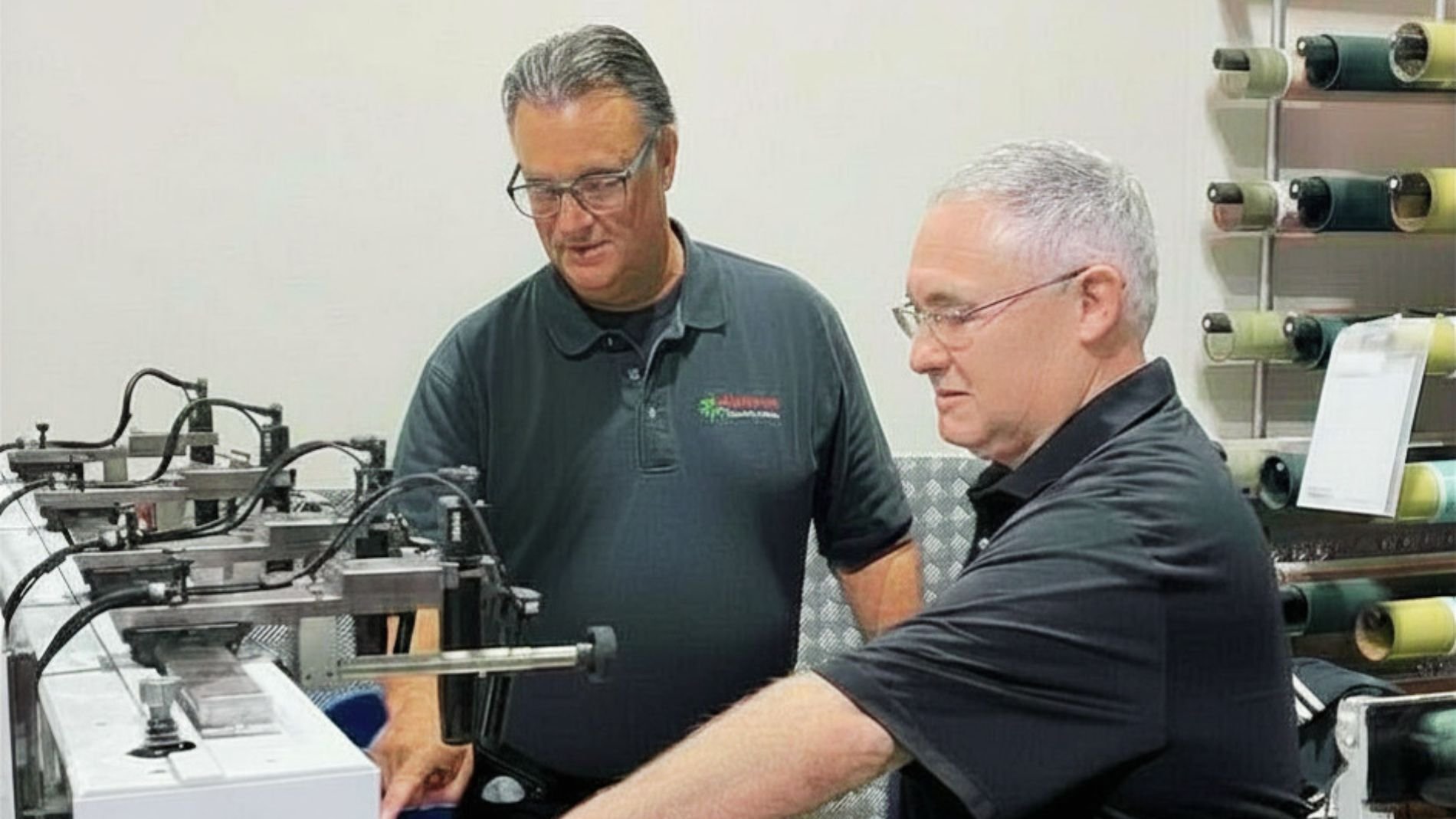 Das Bild zeigt Stan Riches und Brad Windsor vor einer Druckmaschine beim Wissenstransfer.